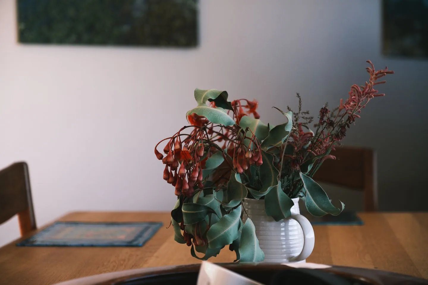Red flowers and leafy stems in a white vase