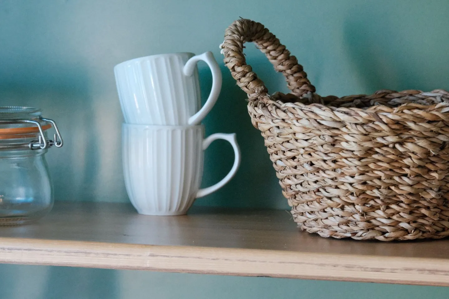 Woven basket beside mugs on an open shelf