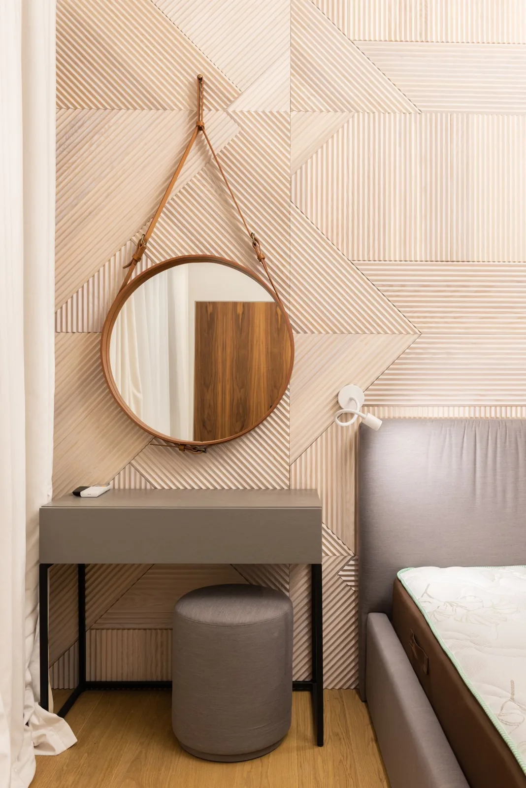 Small dressing table and round mirror beside a bed