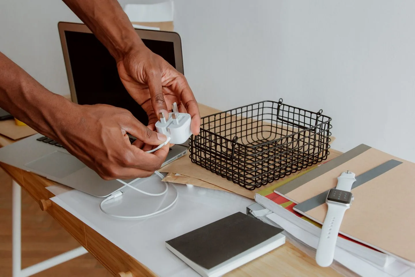 Hands gathering a charging cable beside a desk basket